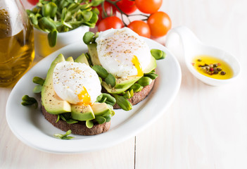 Avocado toast, cherry tomato on wooden background. Breakfast with toast avocado, vegetarian food, healthy diet concept. Healthy sandwich with avocado and poached eggs.