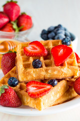 Photo of fresh homemade food made of berry Belgian waffles with honey, chocolate, strawberry, blueberry, maple syrup and cream. Healthy dessert breakfast concept with juice. 