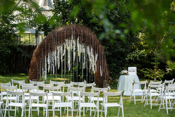 Wedding day. Amazing place for the ceremony. Wedding arch with crystal elements and wood, white chairs. In the park.