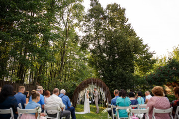 Obraz premium Wedding. Rustic wedding. Bride and groom near the wedding arch at the wedding ceremony, guests on chairs looking on newlyweds couple