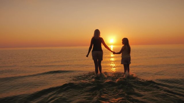 Mom and daughter are walking on the water against the backdrop of the setting sun