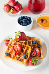 Photo of fresh homemade food made of berry Belgian waffles with honey, chocolate, strawberry, blueberry, maple syrup and cream. Healthy dessert breakfast concept with juice. 