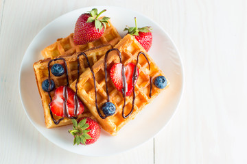 Photo of fresh homemade food made of berry Belgian waffles with honey, chocolate, strawberry, blueberry, maple syrup and cream. Healthy dessert breakfast concept with juice. 