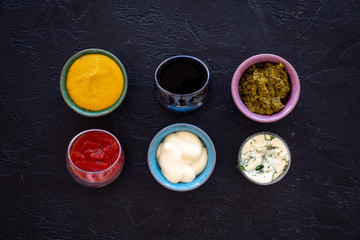Set of sauces. Ketchup, mayonnaise, mustard, soy sauce, barbecue sauce, pesto, mustard, sour with greenery on black background top view copy space
