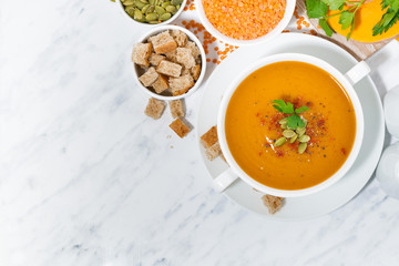 soup of pumpkin and lentils in a bowl on white background, top view