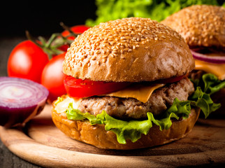 Close-up photo of home made hamburger with beer made of beef, onion, tomato, lettuce, cheese and spices. Fresh burger closeup on wooden rustic table with potato fries and chips.