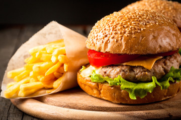 Close-up photo of home made hamburger with beer made of beef, onion, tomato, lettuce, cheese and spices. Fresh burger closeup on wooden rustic table with potato fries and chips.