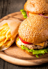 Close-up photo of home made hamburger with beer made of beef, onion, tomato, lettuce, cheese and spices. Fresh burger closeup on wooden rustic table with potato fries and chips.
