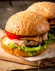 Close-up photo of home made hamburger with beer made of beef, onion, tomato, lettuce, cheese and spices. Fresh burger closeup on wooden rustic table with potato fries and chips.