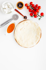 Make pizza concept. Pizza dough and ingredients for filling. Cherry tomatoes, olive oil, cheese mozzarella, spices near knife for pizza on white background top view mockup space for text