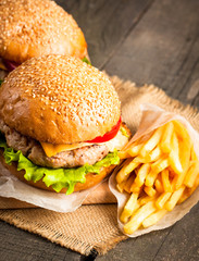 Close-up photo of home made hamburger with beer made of beef, onion, tomato, lettuce, cheese and spices. Fresh burger closeup on wooden rustic table with potato fries and chips.