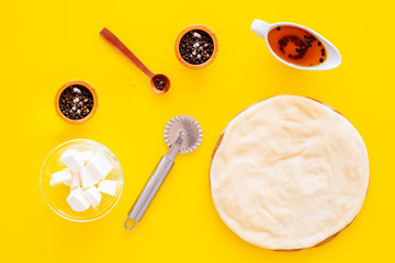 Raw rolled out pizza dough near cheese mozzarella, olive oil, spices, knife for pizza on yellow background top view mockup