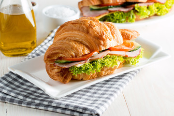Fresh croissant or sandwich with salad, ham, jamon, prosciutto, salami, cheese, chicken, tomatoes on wooden background. Morning breakfast concept. Healthy and fast food.