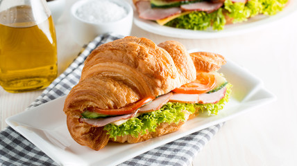 Fresh croissant or sandwich with salad, ham, jamon, prosciutto, salami, cheese, chicken, tomatoes on wooden background. Morning breakfast concept. Healthy and fast food.