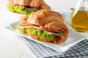Fresh croissant or sandwich with salad, ham, jamon, prosciutto, salami, cheese, chicken, tomatoes on wooden background. Morning breakfast concept. Healthy and fast food.