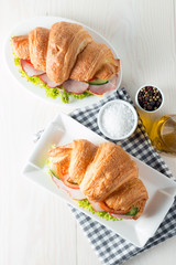 Fresh croissant or sandwich with salad, ham, jamon, prosciutto, salami, cheese, chicken, tomatoes on wooden background. Morning breakfast concept. Healthy and fast food.