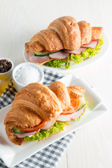 Fresh croissant or sandwich with salad, ham, jamon, prosciutto, salami, cheese, chicken, tomatoes on wooden background. Morning breakfast concept. Healthy and fast food.