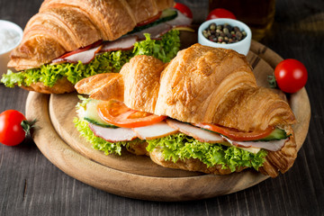 Fresh croissant or sandwich with salad, ham, jamon, prosciutto, salami, cheese, chicken, tomatoes on wooden background. Morning breakfast concept. Healthy and fast food.