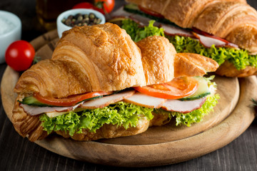 Fresh croissant or sandwich with salad, ham, jamon, prosciutto, salami, cheese, chicken, tomatoes on wooden background. Morning breakfast concept. Healthy and fast food.