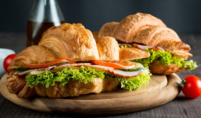 Fresh croissant or sandwich with salad, ham, jamon, prosciutto, salami, cheese, chicken, tomatoes on wooden background. Morning breakfast concept. Healthy and fast food.