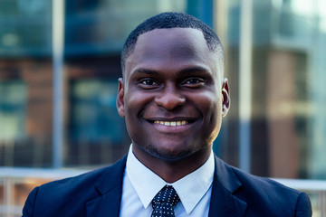 Fototapeta premium portrait of beautiful and stylish African American man in a fashionable black jacket and a white shirt with a collar with a elegant tie smileing background of Manhattan glass offices cityscape