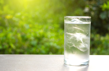 Glass of ice and water in put on table in the nature green background