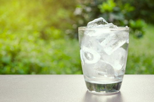 Glass of ice and water in put on table in the nature green background
