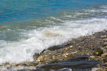 pebble stones on the sea beach, the rolling waves of the sea with foam