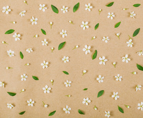 Floral pattern made of white spring flowers, buds and green leaves on brown paper background. Flat lay. Top view.