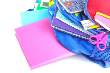 Many different stationery and school supplies lying in a school backpack on a white isolated background