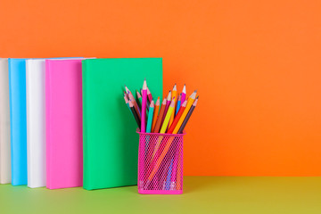 Books and a glass with colored pencils on a bright orange and green background with a place for writing