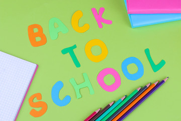 Stationery and multi-colored inscription back to schooll on a bright green background