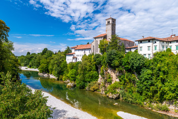 Fototapeta na wymiar Cividale del Friuli, Italy: View of the old city center with traditional architecture. River Natisone with transparent water. Summer day and blue sky with clouds.