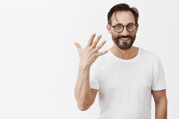 See no ring yet. Portrait of charming joyful and carefree bachelor in trendy glasses with nice short hairstyle showing five with raised palm and smiling broadly, being in great mood on summer day