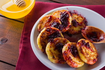 Cottage cheese pancakes on a wooden background. Traditional Ukrainian dish - syrniki with jam on a red napkin. Pancakes with cottage cheese on a white plate with honey and rowan. Copy space