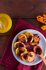Cottage cheese pancakes on a wooden background. Traditional Ukrainian dish - syrniki with jam on a red napkin. Pancakes with cottage cheese on a white plate with honey and rowan. Copy space