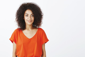 Fototapeta premium Beautiful people and positive emotions concept. Joyful good-looking dark-skinned model with afro hairstyle standing in stylish t-shirt and smiling happily at camera, picking puppy in local shelter