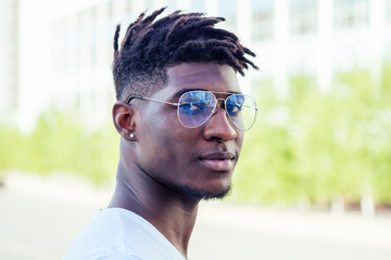 portrait stylish and handsome African student American man with cool dreadlocks and earringin the ear diamond fashion look walking on the street