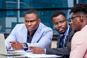 A group of three stylish African American men entrepreneurs in fashion business suits working...