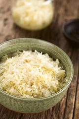 Fresh healthy sauerkraut in bowl with jar in the back, photographed on rustic wood (Selective Focus, Focus one third into the image)