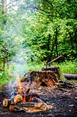 Vertical photo of a fire on the background of a stump with an ax and firewood harvested under it.
