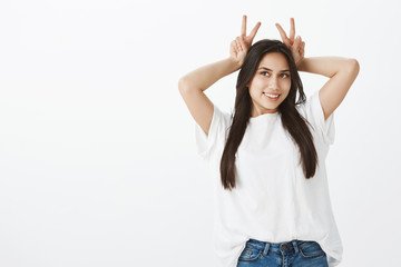 Indoor shot of dreamy flirty female student in casual outfit, raising victory or peace gestures...