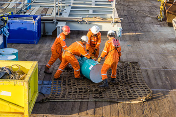 Offshore workers preps oil drum on cargo net on a construction barge at oilfield