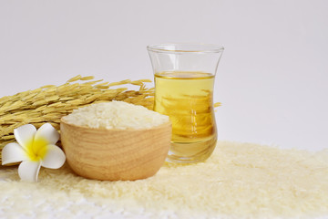 Rice bran oil in a glass with uncooked jasmine rice in a wooden bowl and ear of rice in the back on white background with copy space for text, selective focus