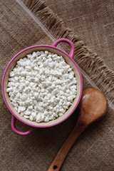 Cottage cheese in a ceramic bowl and a wooden spoon on a background of burlap, homemade rural healthy food