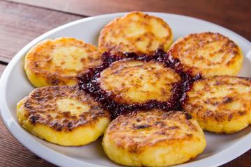 Cottage cheese pancakes on a wooden background. Traditional Ukrainian dish - syrniki with jam and honey. Pancakes with cottage cheese on a white plate. Copy space