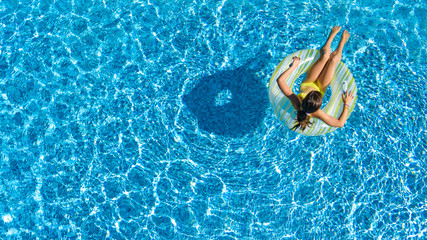 Aerial top view of little girl in swimming pool from above, kid swims on inflatable ring donut ,...