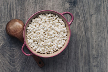 Cottage cheese in a ceramic bowl and a wooden spoon on a wooden background, homemade rural healthy food