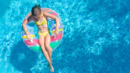 Aerial top view of little girl in swimming pool from above, kid swims on inflatable ring donut , child has fun in blue water on family vacation resort
