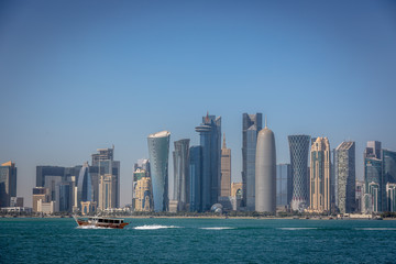 Fototapeta na wymiar The skyline of Doha with a traditional boat in the foreground in Qatar, on a blue sky day, winter time, seen from the MIA Park